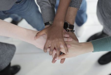 Integration PPC - Crop from above of faceless multiracial friends in casual clothes uniting hands after coming to agreement while standing on light grey ceramic floor