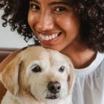 Content Calendar - Young content ethnic female with Afro hairstyle embracing cute purebred dog on couch in house while looking at camera