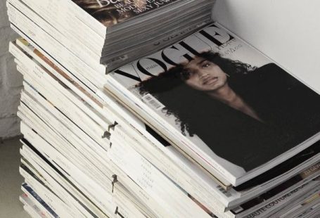Design Trends - High angle many fashion magazines stacked on floor against white brick wall in studio